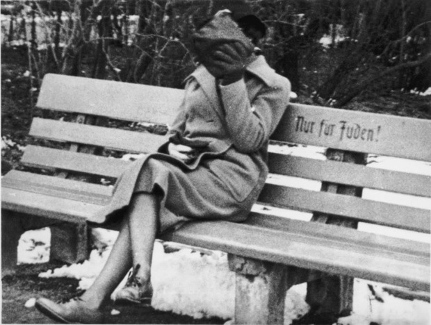 A Jewish woman who is concealing her face sits on a park bench marked Only for Jews, Austria, 1938